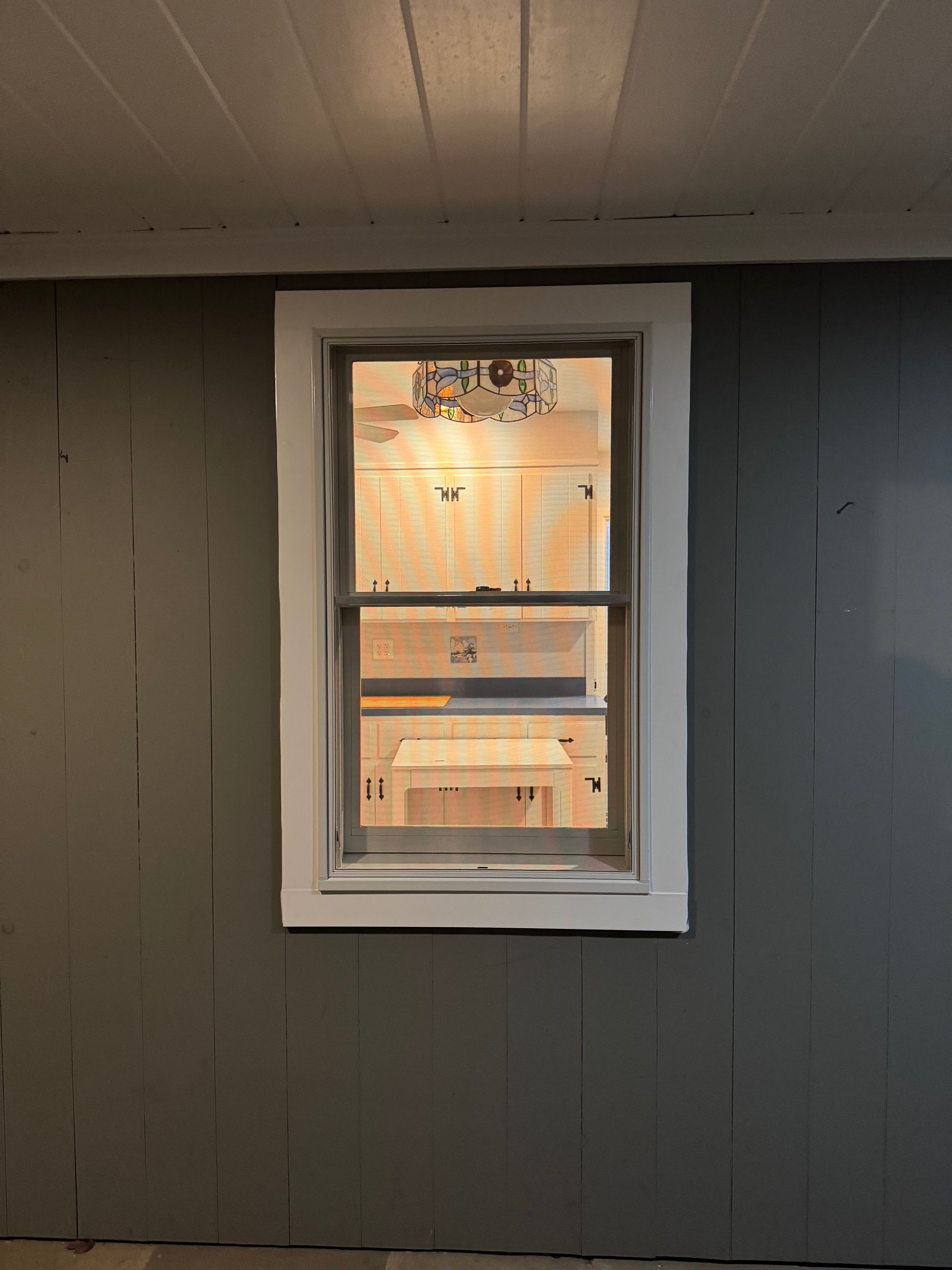 Window with white trim set in gray paneled wall; interior visible.