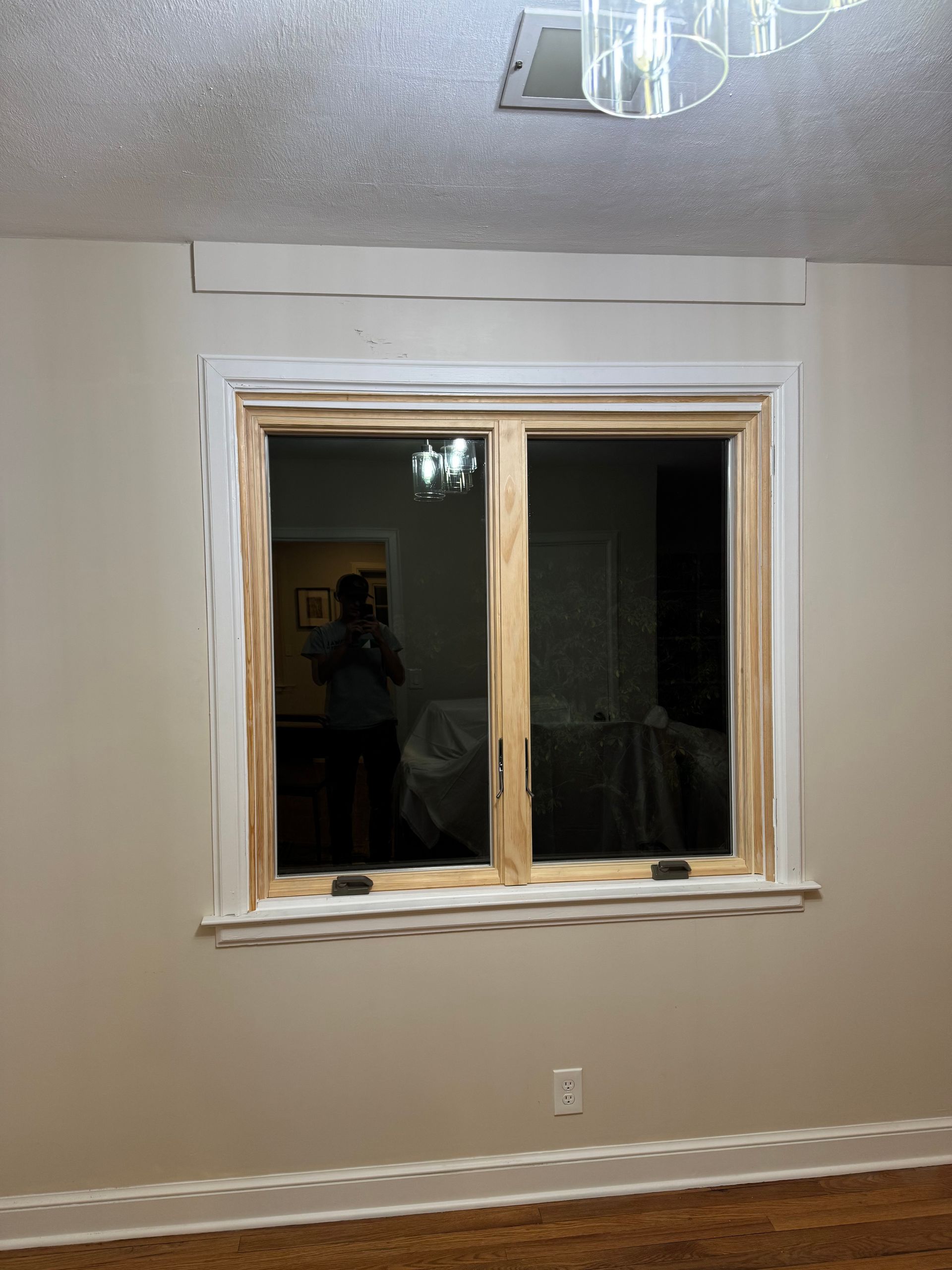 Window in a room with white trim, tan frame, and a person reflected in the glass.