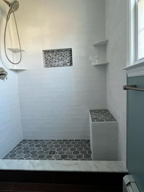 White tiled shower with a gray hexagon floor, built-in bench, and niche.