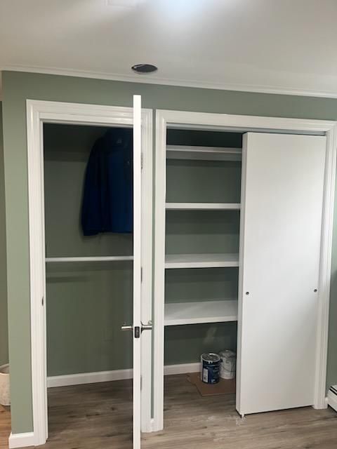 Closet with sliding doors and shelves. Open door reveals hanging coat and shelving. White doors/shelves, green walls.