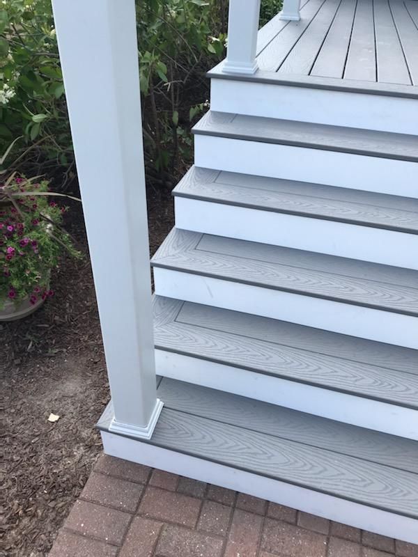 Gray and white outdoor steps leading to a deck, next to a white post and red brick path.