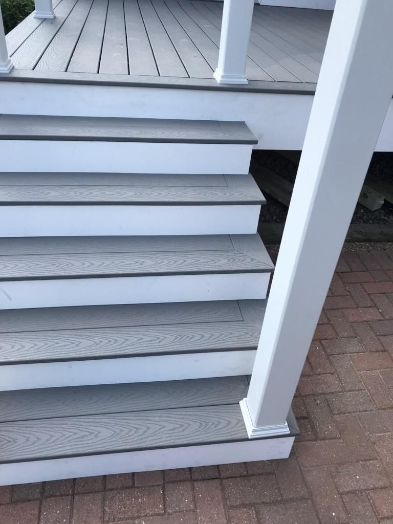 Gray composite steps with white risers lead up to a porch with white railing and posts.