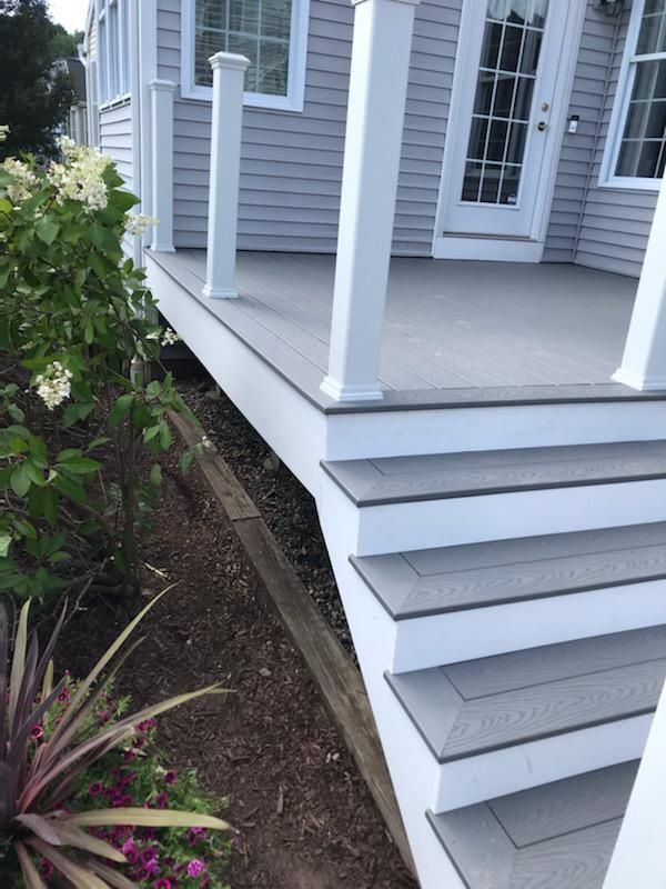Gray and white deck with steps, next to house with plants.