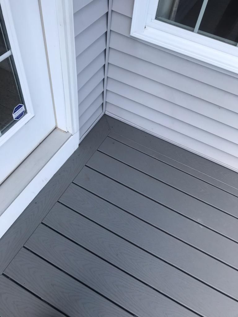 Corner of a gray composite deck, with light gray siding and white door/window trim.