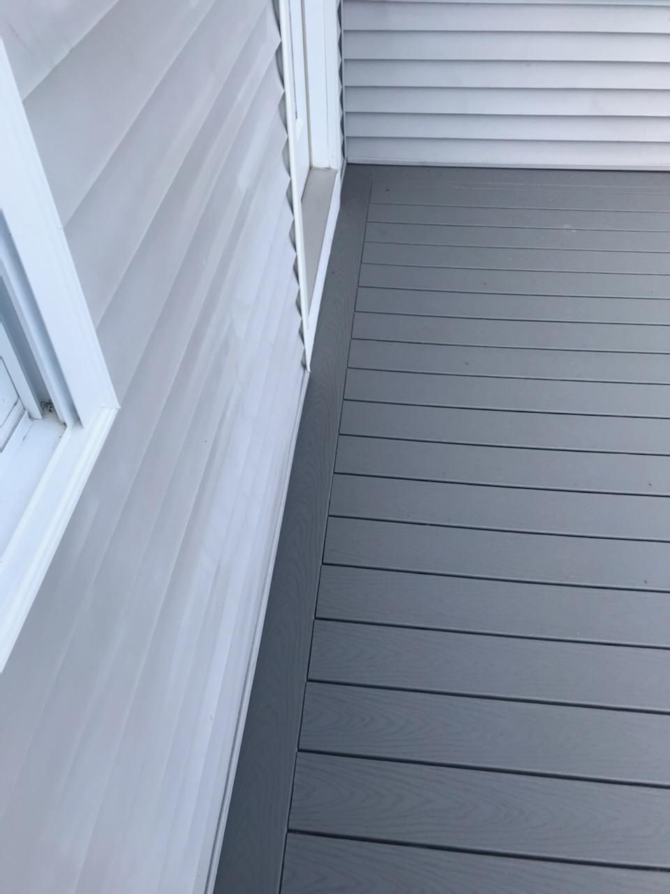 Gray siding next to a gray deck. The siding has white trim near a window.
