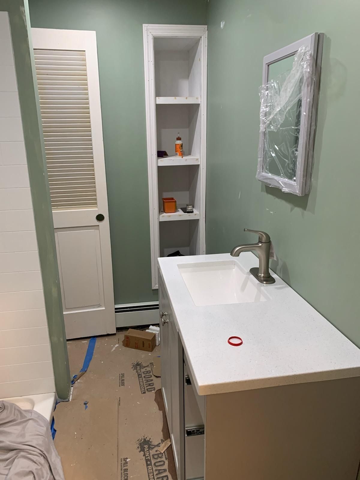 Bathroom with a vanity, mirror, built-in shelves, and door. The walls are green.