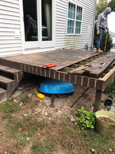 Deck being rebuilt with wood planks removed; a worker stands nearby, ground level.