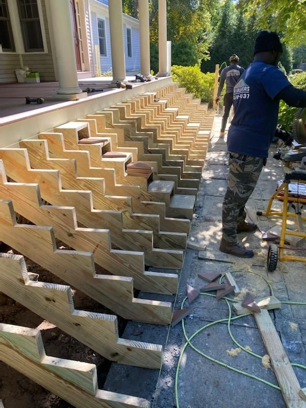 Construction workers building outdoor wooden steps next to a house.