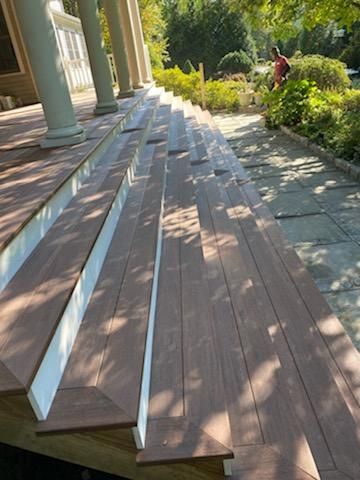 Wooden porch with white trim and columns, steps partially boarded, person working in the background.