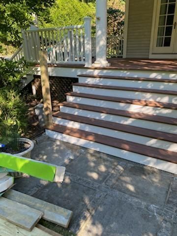 Wooden stairs with white trim lead up to a porch with white railings and columns.