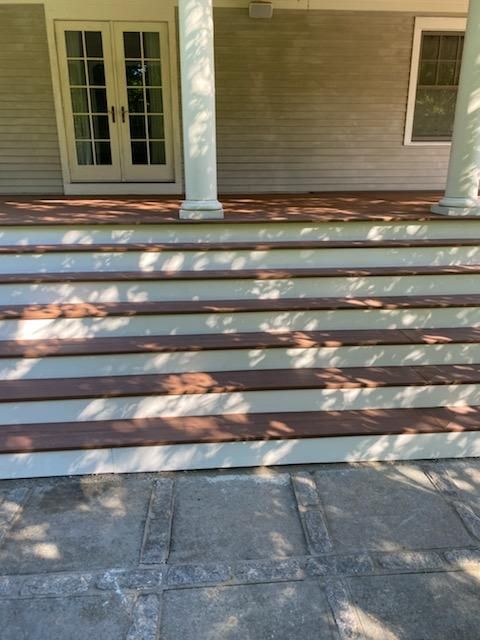 Wooden steps leading up to a house with white trim and pillars. Gray stone patio below.