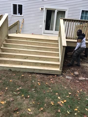 Wooden deck with stairs leading down to a grassy yard; person walking on the side of the deck.
