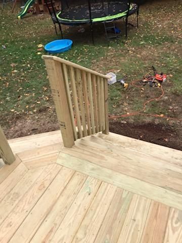 Wooden deck with railing leading to yard. Trampoline and blue tub visible.