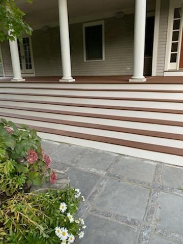 A covered porch with white columns, brown steps, and a gray stone walkway.