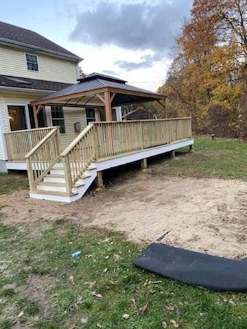 Wooden deck with stairs, gazebo, and house in a grassy yard.