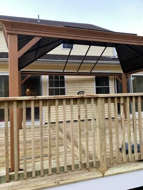 Wooden deck with a brown pergola, next to a pale yellow house.