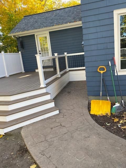 Exterior view: blue house with deck, concrete pathway, and yard tools.