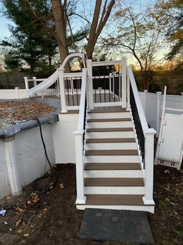 White and brown deck with stairs, a slide, and a black and white fence surrounding a pool.