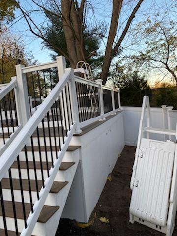 Outdoor deck with stairs, black railing, and white wall, next to a pool area with a ladder.