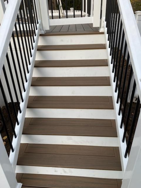 Staircase with brown treads and white risers, black railing posts, and white handrails.