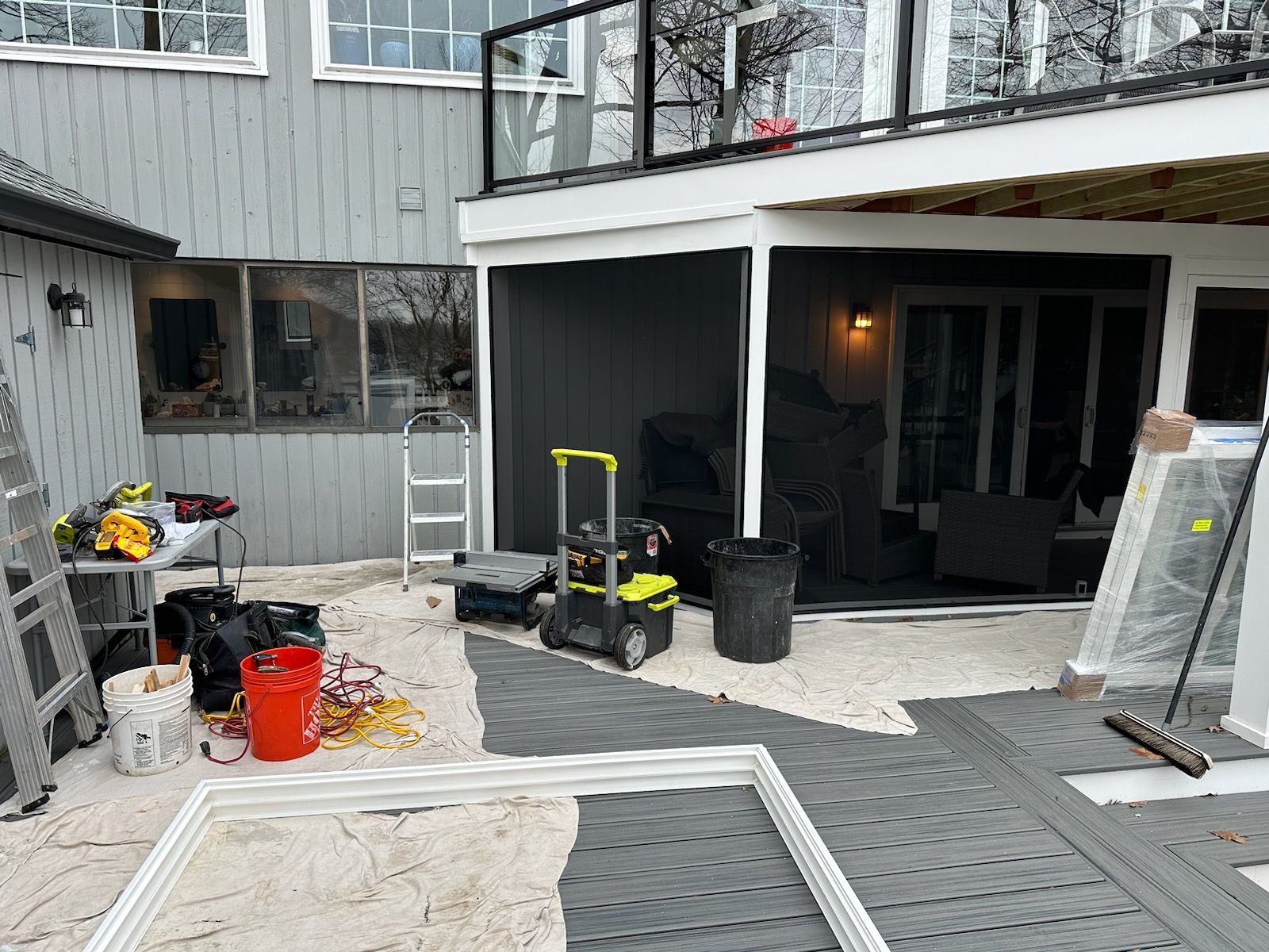 Exterior renovation scene: gray house with deck, tools, and construction materials.