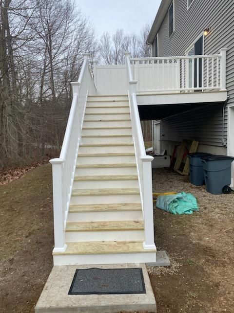 White outdoor staircase leading to a deck, set against a house and yard.