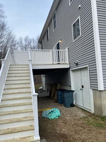 Exterior of a two-story house with a deck and stairs. Light gray siding, white railings and stairs.