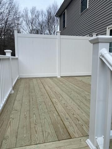 Wooden deck with white vinyl fence and railing against a gray house.