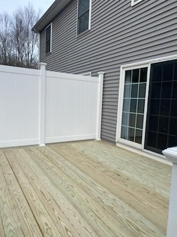 Wooden deck with a white vinyl fence and a sliding glass door against a gray house.