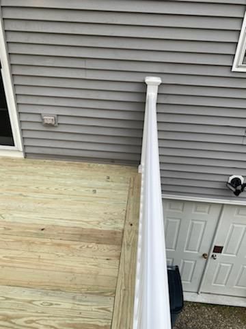 Wooden deck with white railing next to a gray-sided building.