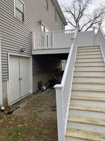 Exterior view of a two-story house with a deck and stairs. White deck railing and staircase. Gray siding.