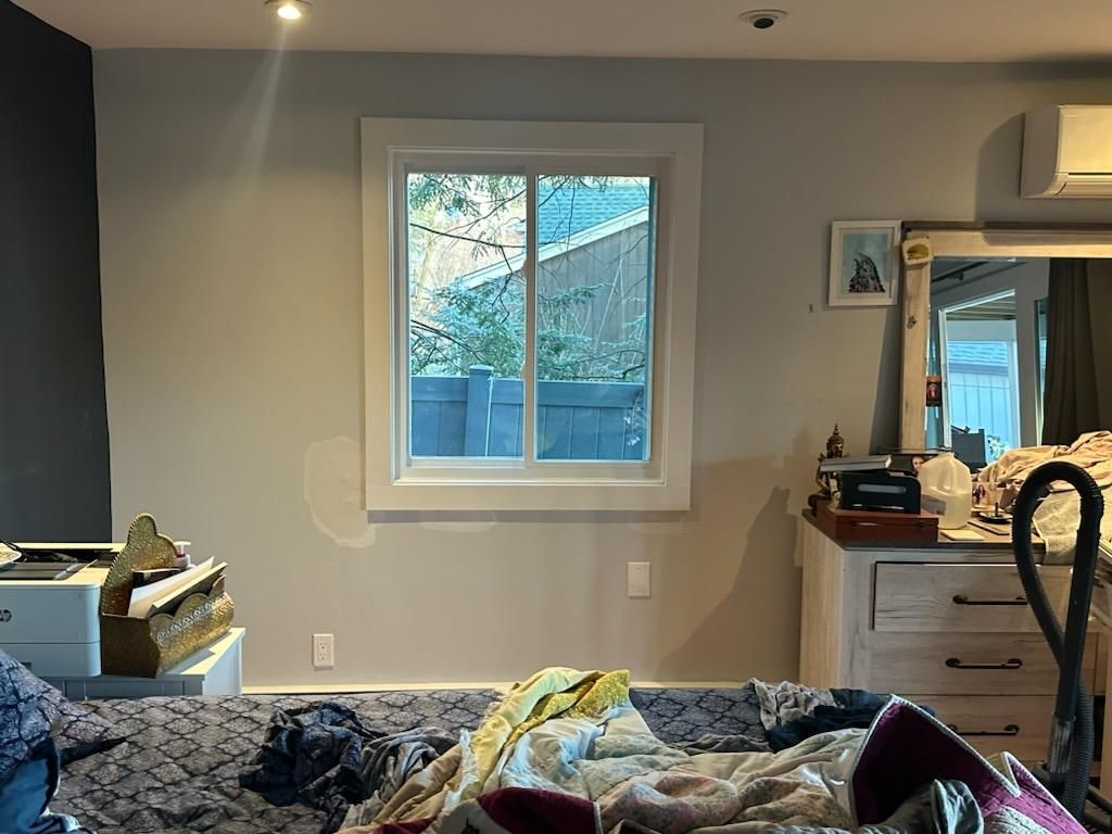 A bedroom with a window, unmade bed, dresser, and wall-mounted air conditioner.
