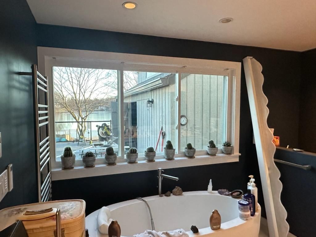 Bathroom with bathtub under a window with cacti. Dark blue walls, white trim, outdoor view.