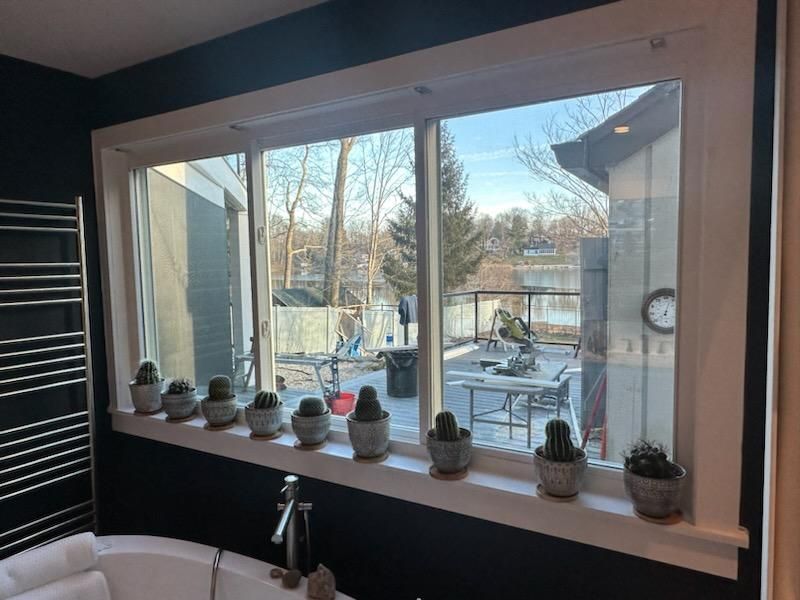 Bathroom window with cactuses on the ledge, overlooking a backyard with patio furniture and a lake view.