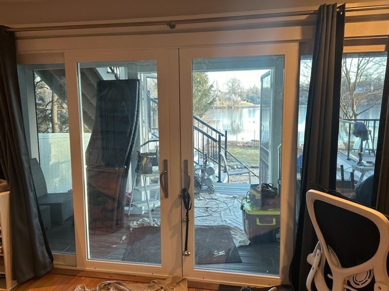 White framed French doors open to a view of a lake and deck. Gray curtains frame the doors.