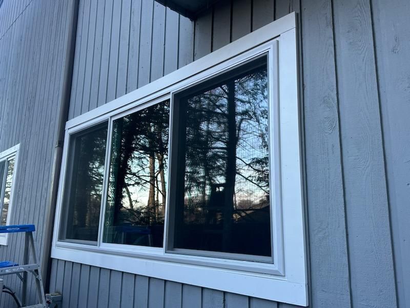 Exterior view of a house with a white-framed sliding glass window. The siding is gray.