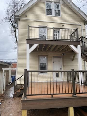 Two-story house with decks; exterior view. Brown decking and railings, white door, light yellow siding, stairs.