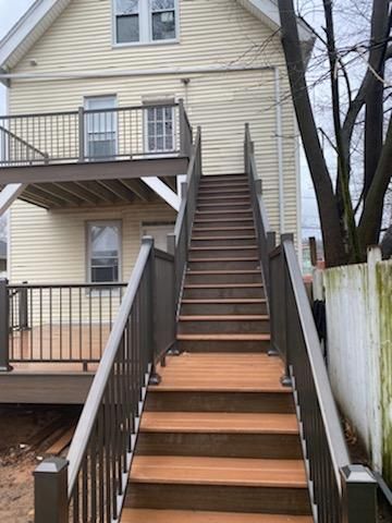 Wooden staircase leading up to a two-story deck attached to a light yellow house.