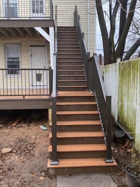 Outdoor staircase with composite steps and railing leading to a deck on a two-story building.