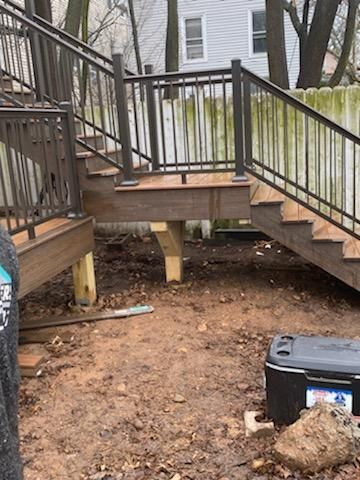 Wooden deck with stairs, metal railings, and bare dirt ground.
