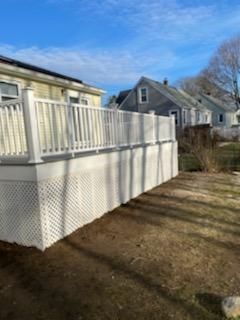White deck with lattice skirting and railing, attached to a yellow house, in a yard with other houses in the background.