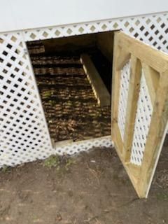 Open access door to crawlspace under a house, door is white with diamond-shaped lattice.