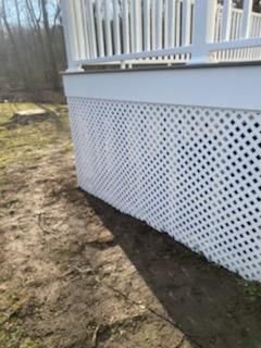 White lattice skirting on a raised deck, viewed from ground level, on a patch of dirt and grass.