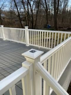 White railing on a gray deck, with trees in the background.