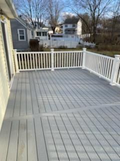 Gray composite deck with white railing, viewed from a doorway, with houses and trees in the background.