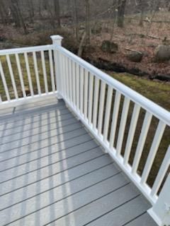 White railing on gray deck overlooking woods.