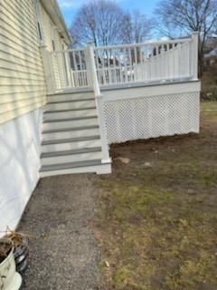 White deck with stairs, lattice skirting, and gray steps against a yellow house.