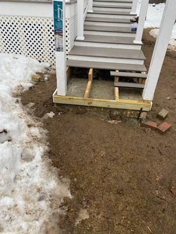 Wooden stairs under construction; framing visible below the steps. Snow and dirt surround the base.