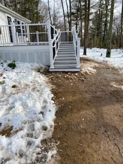 White deck with stairs, partially melted snow on ground. Brown dirt path leads away from stairs.
