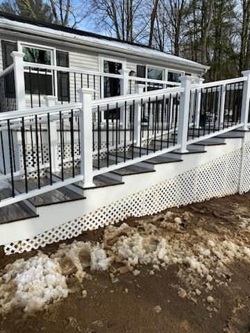 Ramp and steps with white railings and black bars leading to a house with windows. Snow on the ground.